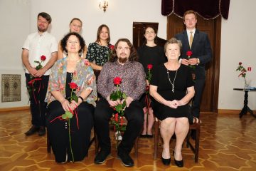 Zdjęcie osób siedzących na krzesłach, każda z nich trzyma czerwoną różę