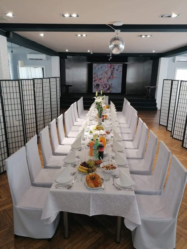 Na zdjęciu wnętrze kawiarni Klubowa, zastawiony potrawami stół, dookoła stoją białe krzesła.