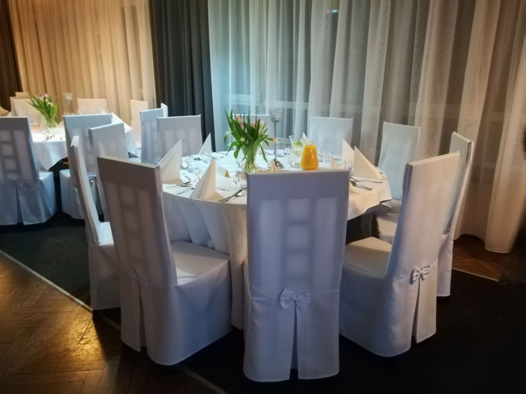 Na zdjęciu wnętrze kawiarni Klubowa, 2 świeżo zastawione okrągłe stoliki, dookoła stoją białe krzesła.