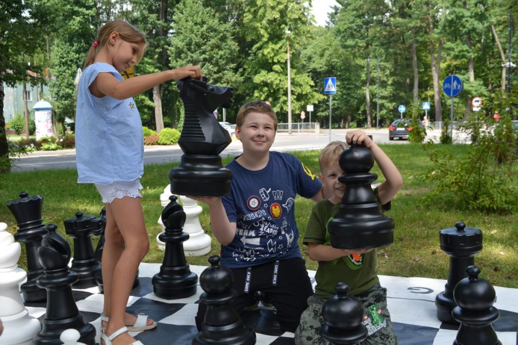 zdjęcie troje dzieci trzyma duże figury szachowe w tle zielone drzewa