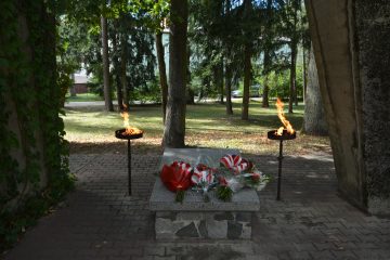 pomnik, kwiaty, dwie świece, w tle drzewa