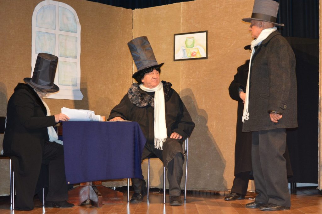 zdjęcie przedstawia aktorów na scenę, ubranych w płaszcze i czarne kapelusze