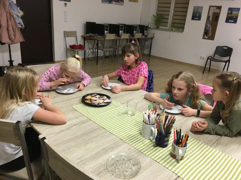 zdjęcie przedstawia dzieci siedzące przy stole, jedzące ciastka