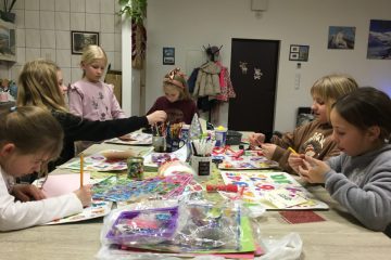 zdjęcie przedstawia stół z artykułami plastycznymi, przy stole siedzą dzieci